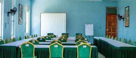 A conference room with green chairs and tables, a whiteboard, and a chandelier.