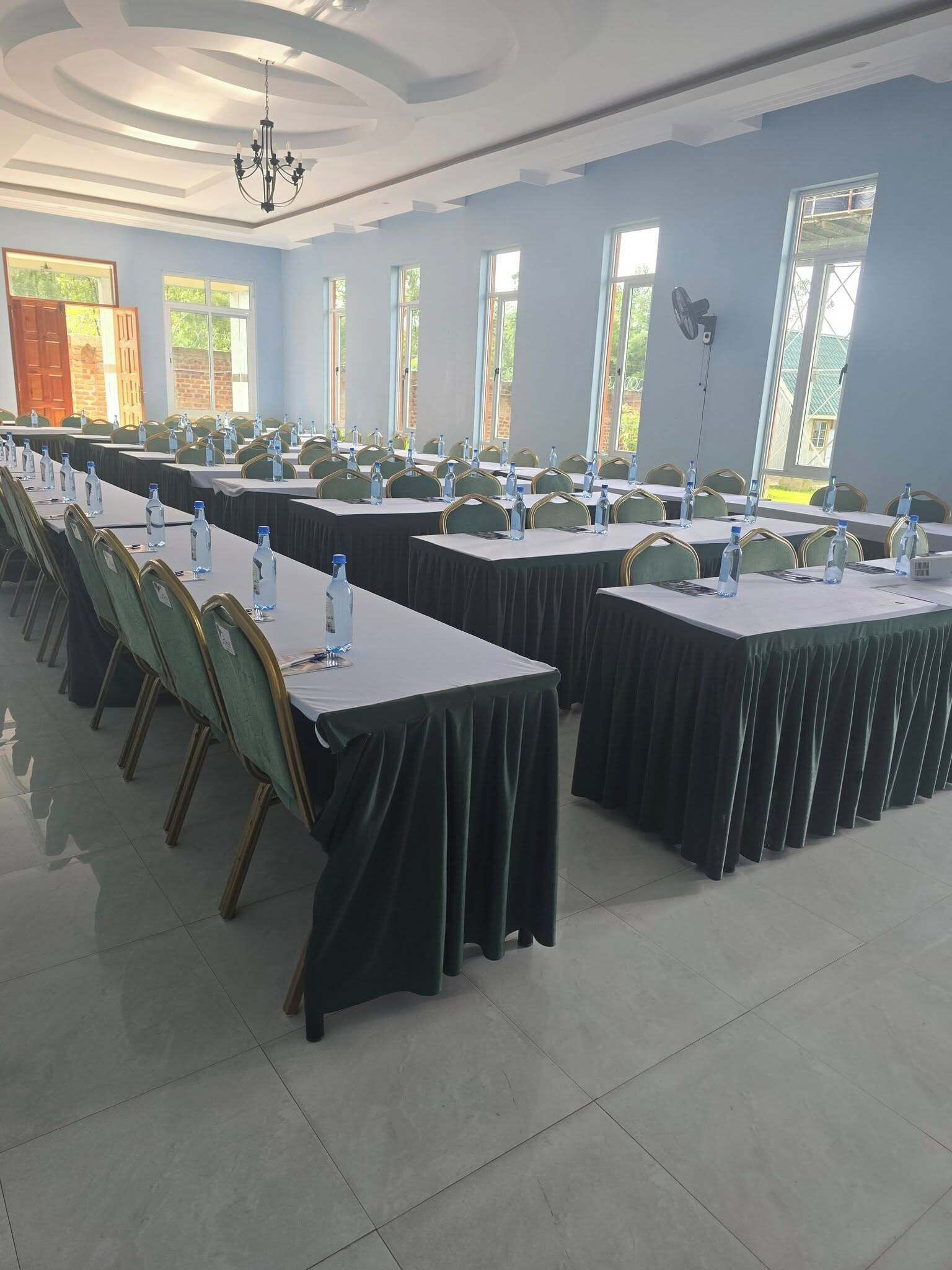 Uma sala de conferências com várias mesas, cadeiras e garrafas de água, com grandes janelas e um candelabro.