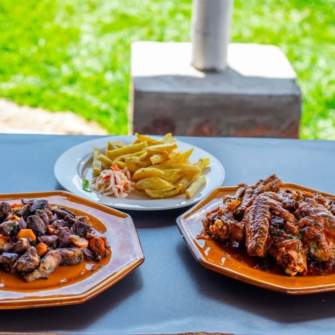 Ein Tisch mit drei Gerichten: ein Fleischgericht mit Gemüse, eine Portion Pommes mit Krautsalat und eine Portion Fleisch mit Soße.