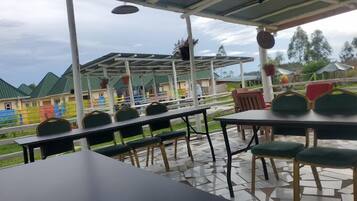 An outdoor patio with tables and chairs, a covered seating area, and a view of colorful buildings in the background.