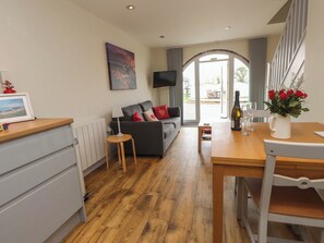 A modern living room with a sofa, a coffee table, and a TV. There is a dining table with a bottle and glasses on it. - Bwthyn Mair (Llangefni)