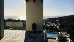 A balcony with a view of a coastal landscape, a swimming pool, and a potted plant. - Architect-designed house with sea and mountain views (Bastia)
