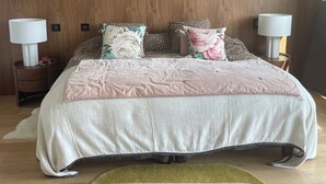 A bedroom with a wooden wall, a bed with floral and leopard print pillows, two bedside tables with lamps, and a circular rug on the floor. - Architect-designed house with sea and mountain views (Bastia)