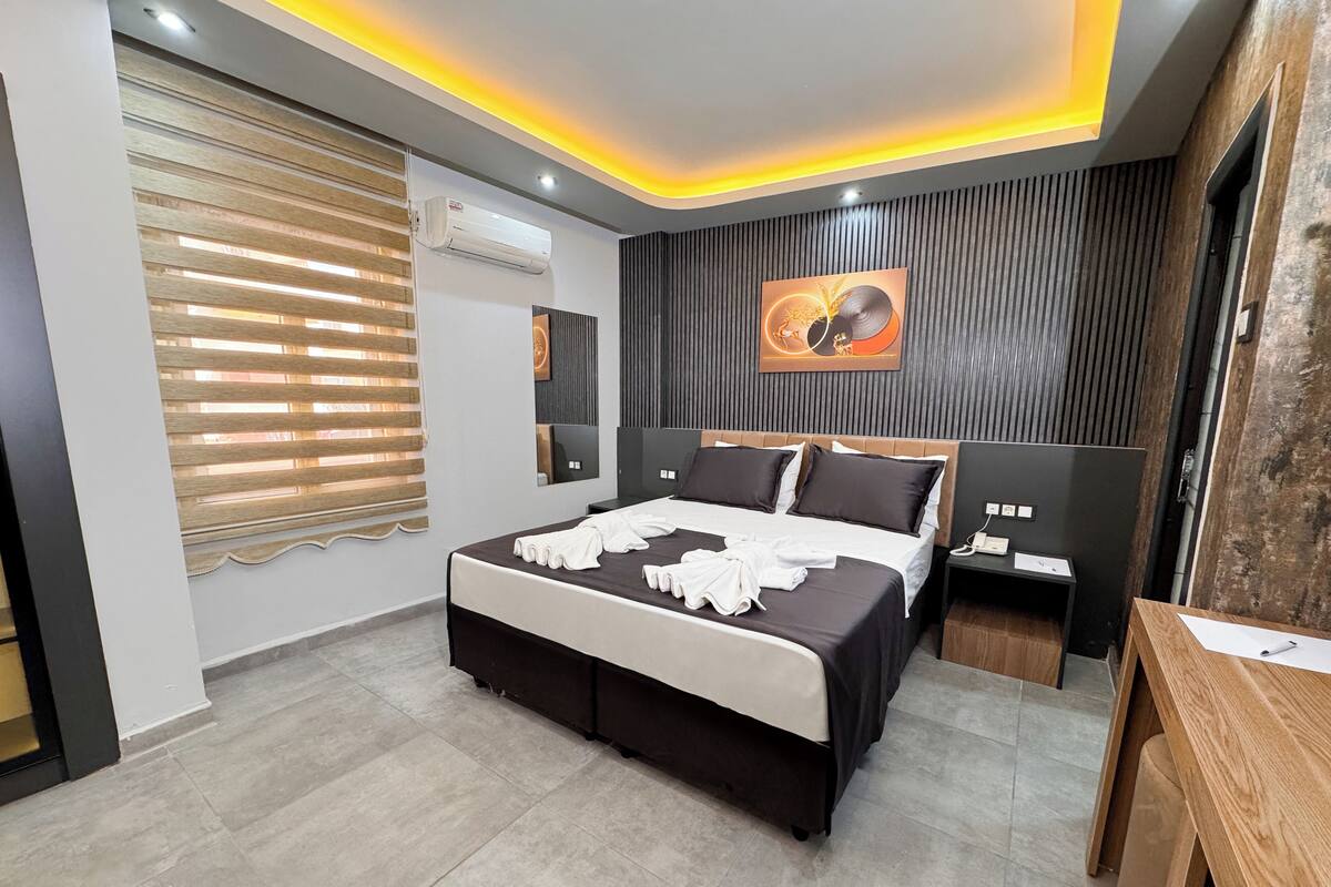 A modern bedroom with a large bed, bedside tables, a desk, and a wall-mounted air conditioner.