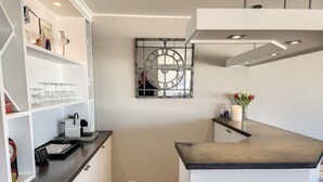 A modern kitchen with white cabinetry, a black countertop, and a wall-mounted clock. - Apartment Albertstrand With Stunning Seafront View (Knokke-Heist)