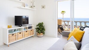 A modern living room with a TV, white shelves, and a balcony with a view of the sea. - Alojamiento vacacional en Caletillas (Candelaria)