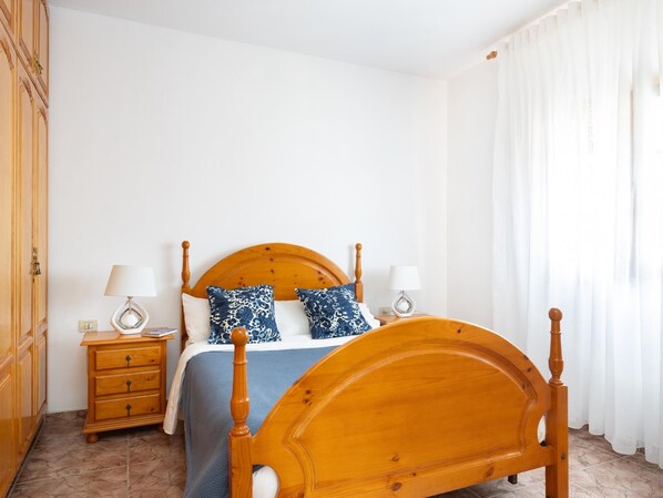 A bedroom with a wooden bed, two bedside tables with lamps, a wardrobe, and a large window with white curtains. - Relax in Candelaria. (Candelaria)