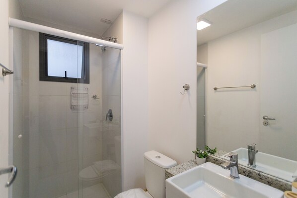 A modern bathroom with a glass-enclosed shower, a white toilet, and a sink with a mirror above it. - Klabin Paulista Studios (Sao Paulo)