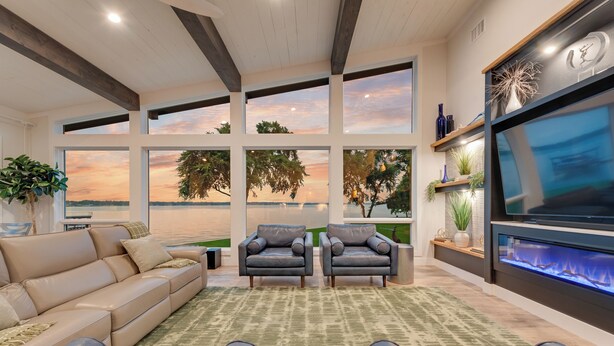 A modern living room with a large sofa, two armchairs, a fireplace, and large windows offering a scenic view.