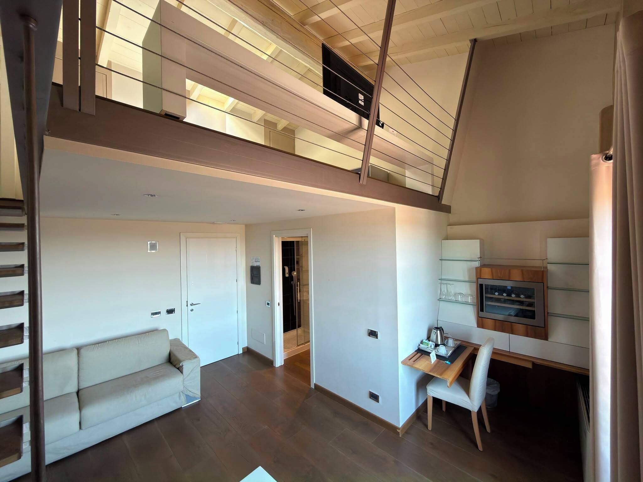 A spacious loft with a high ceiling, a staircase, a sofa, a dining area, and a kitchen.