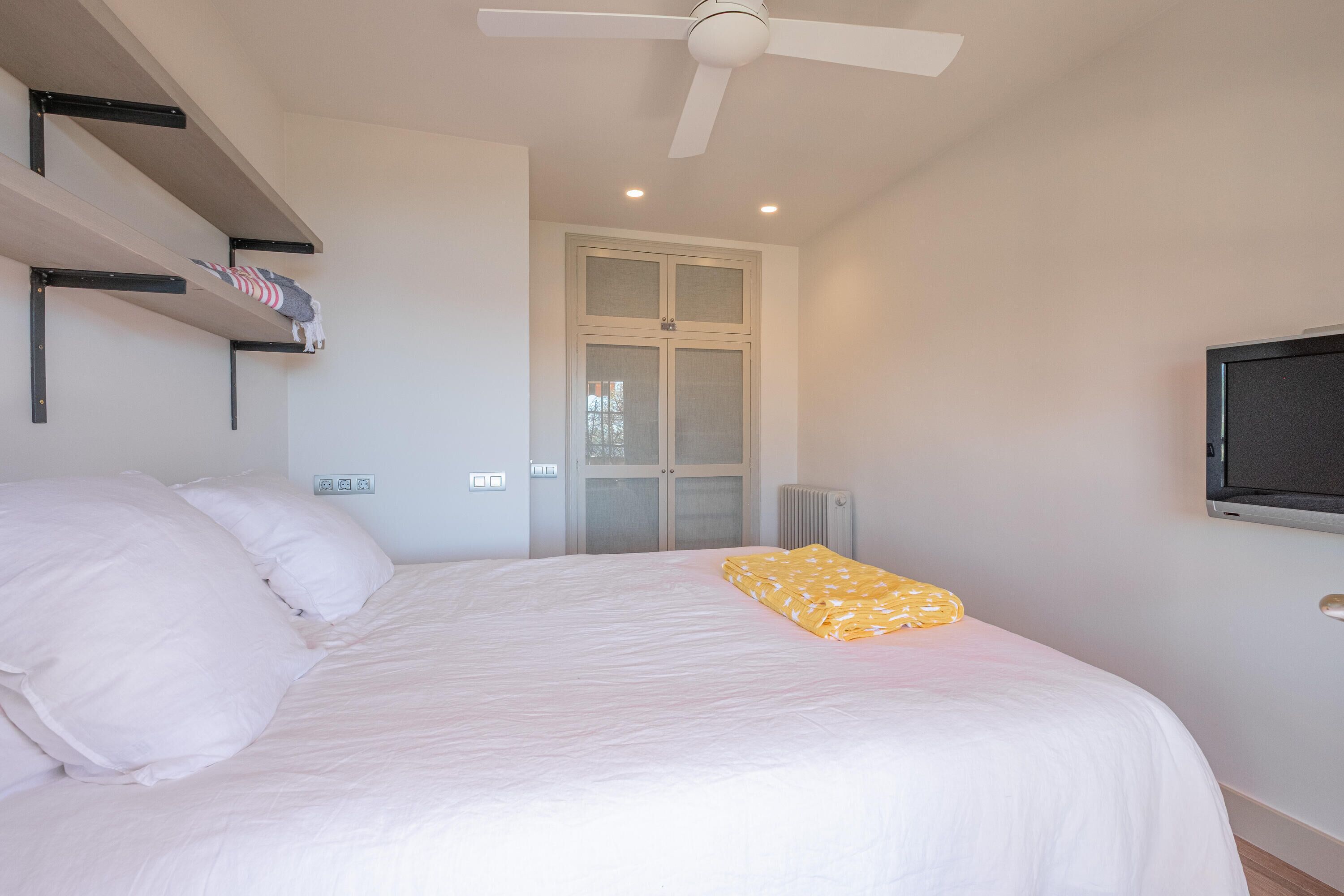 Ein Schlafzimmer mit Bett, Deckenventilator, Fernseher und Fenster.