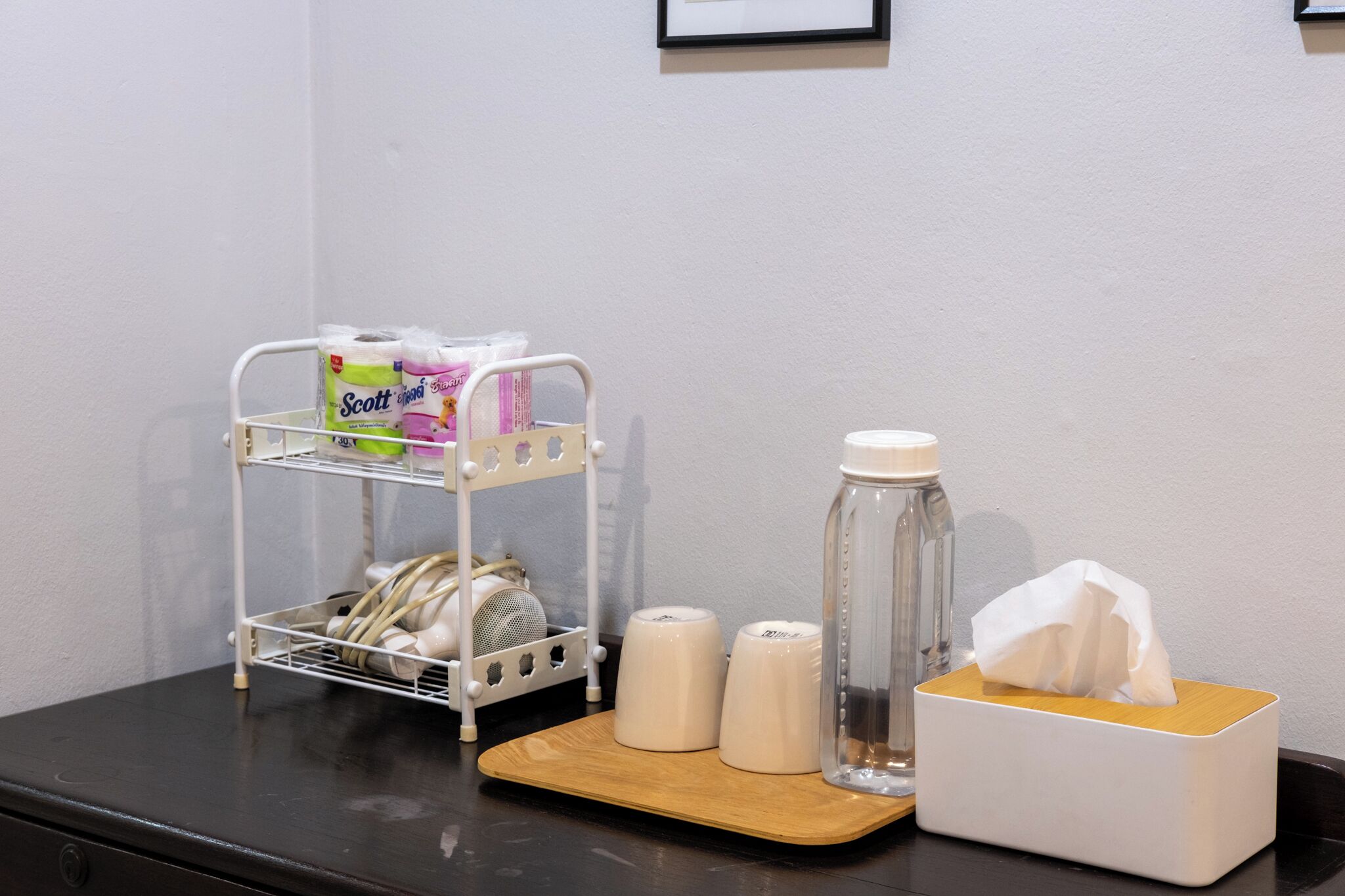 A small table with a tissue box, a water bottle, and a white shelf with toiletries.