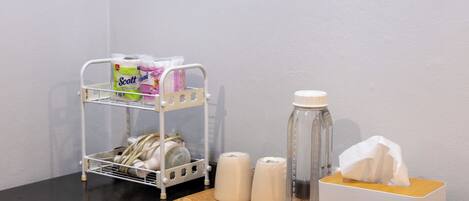 A small table with a tissue box, a water bottle, and a white shelf with toiletries.