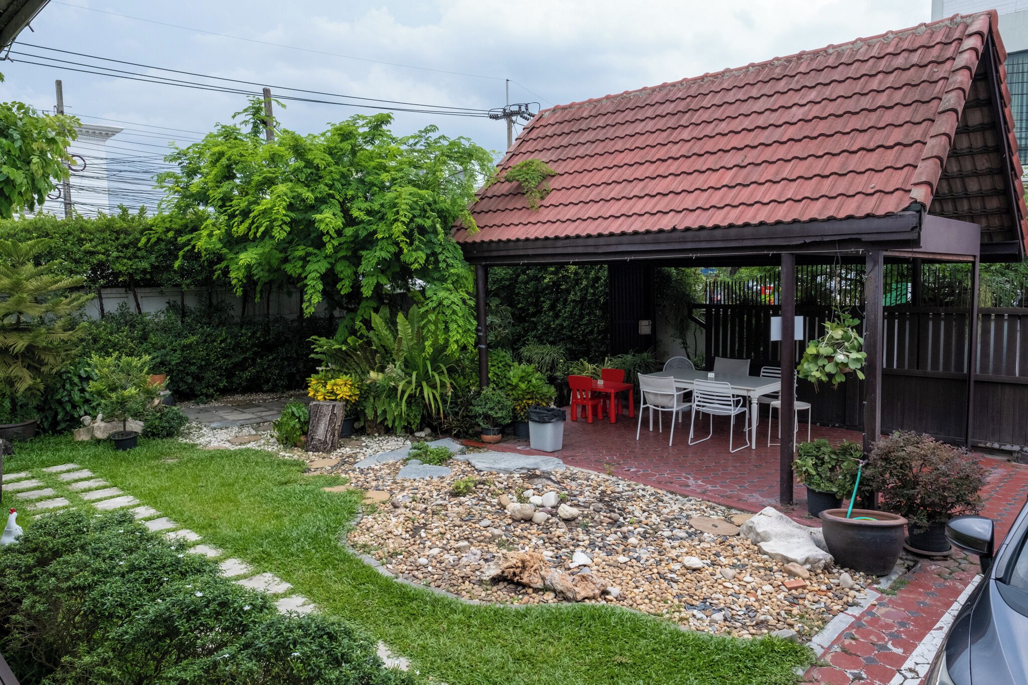 A patio area with a covered seating space, surrounded by a garden with various plants and a gravel path.