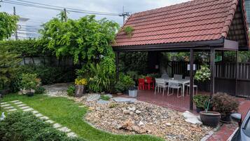 A patio area with a covered seating space, surrounded by a garden with various plants and a gravel path.