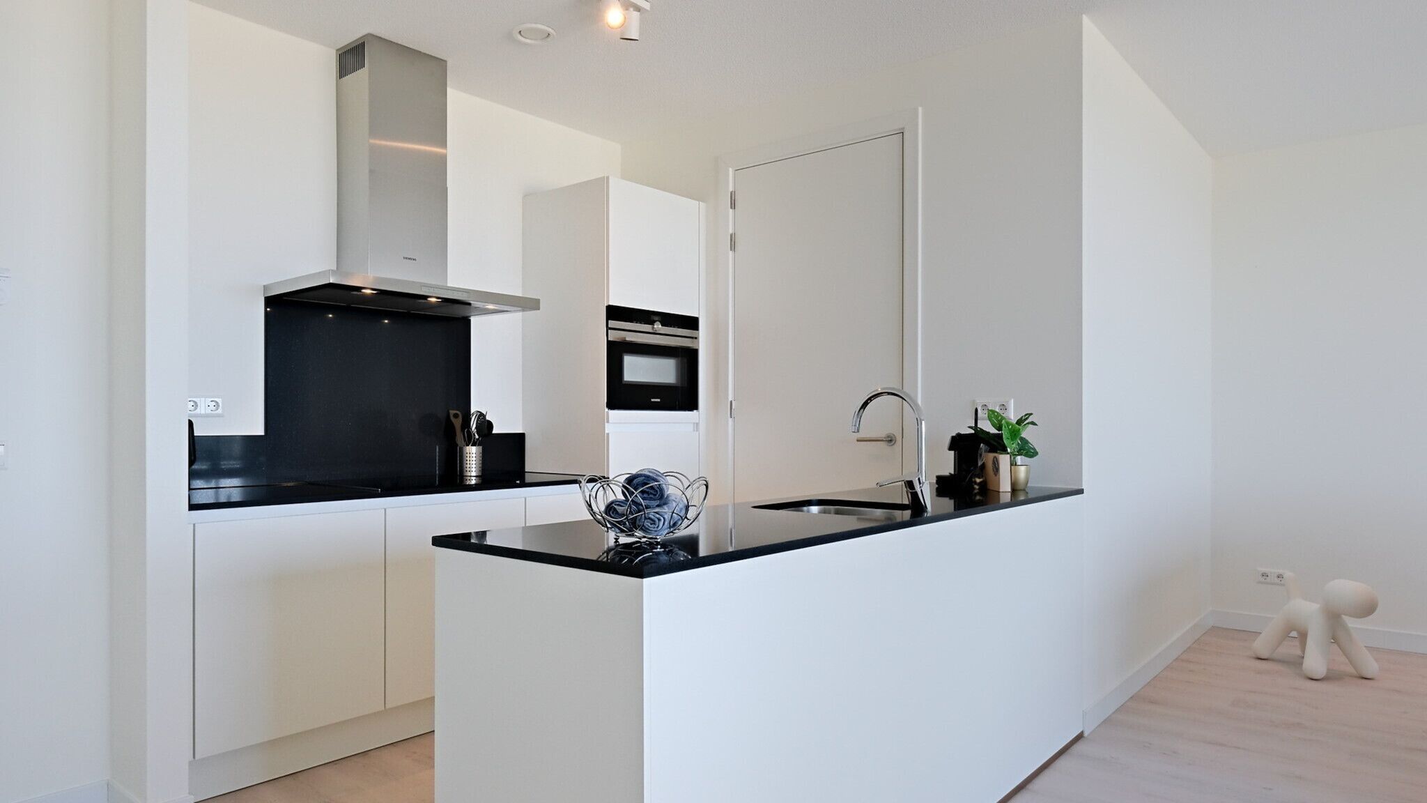 A modern kitchen with white cabinetry, black countertops, a stainless steel range hood, and a built-in oven.