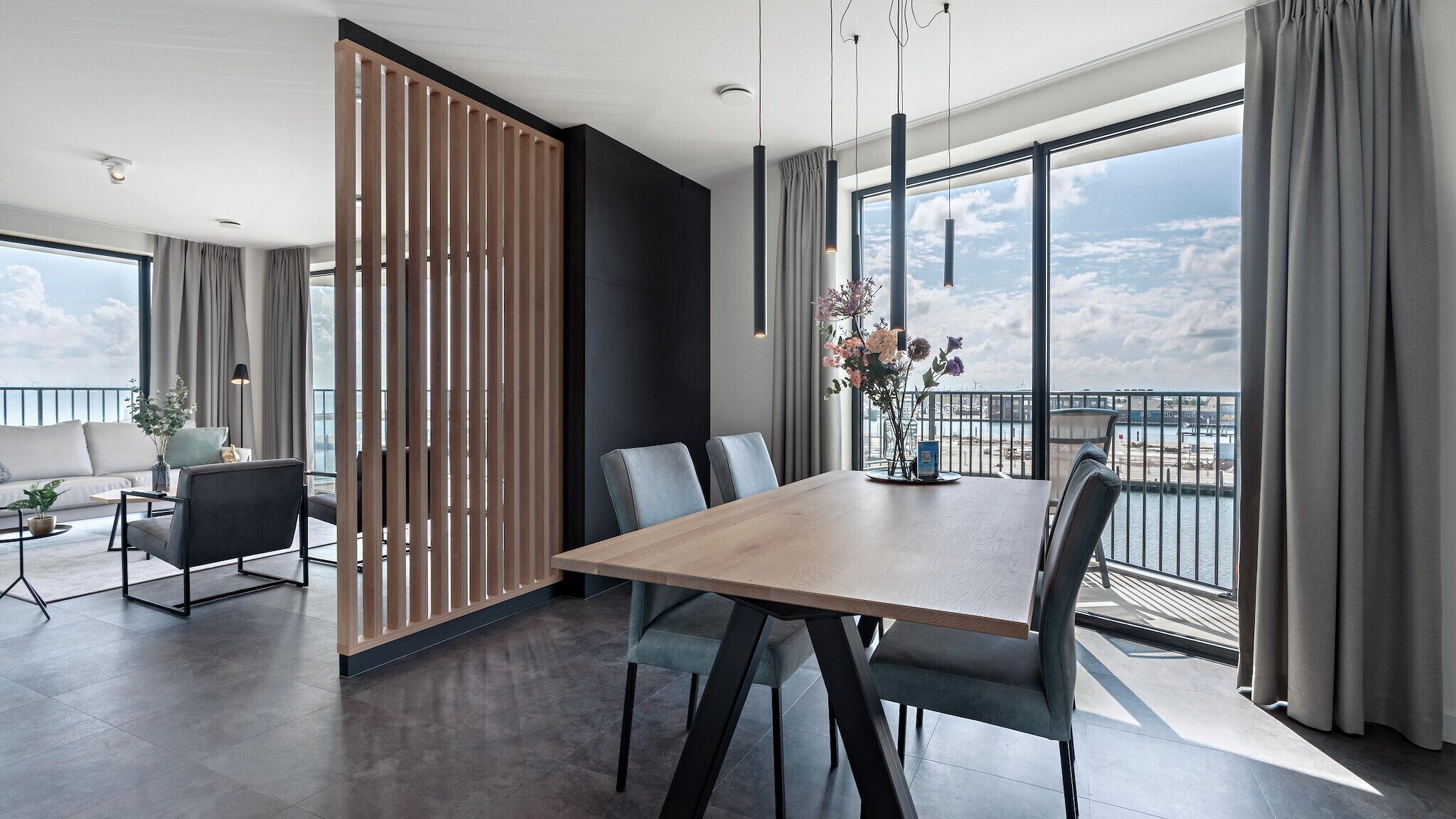 Habitación de hotel moderna con un balcón grande, un comedor con mesa de madera y vistas a la ciudad.
