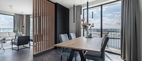 Habitación de hotel moderna con un balcón grande, un comedor con mesa de madera y vistas a la ciudad.