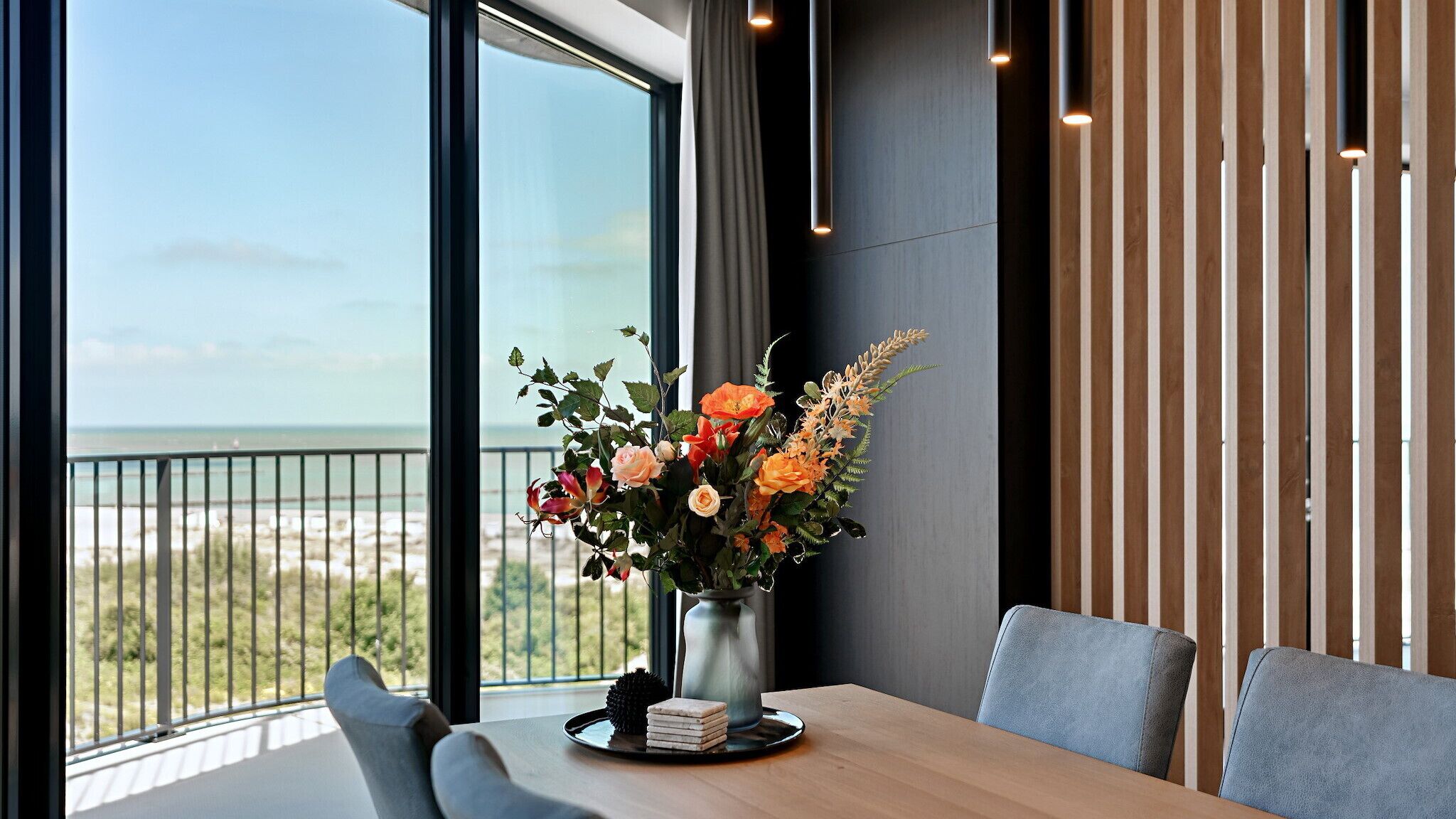 Un comedor con vistas a la playa, un jarrón de flores y una decoración interior moderna.
