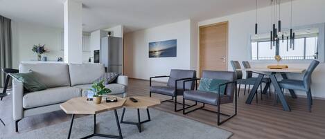 A modern living room with a sofa, two armchairs, a coffee table, and a dining area with a table and chairs.