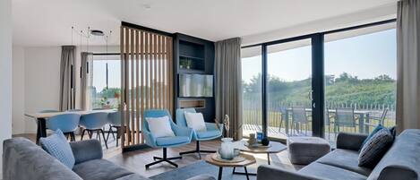 A modern living room with grey sofas, blue armchairs, and a dining area with a table and chairs.