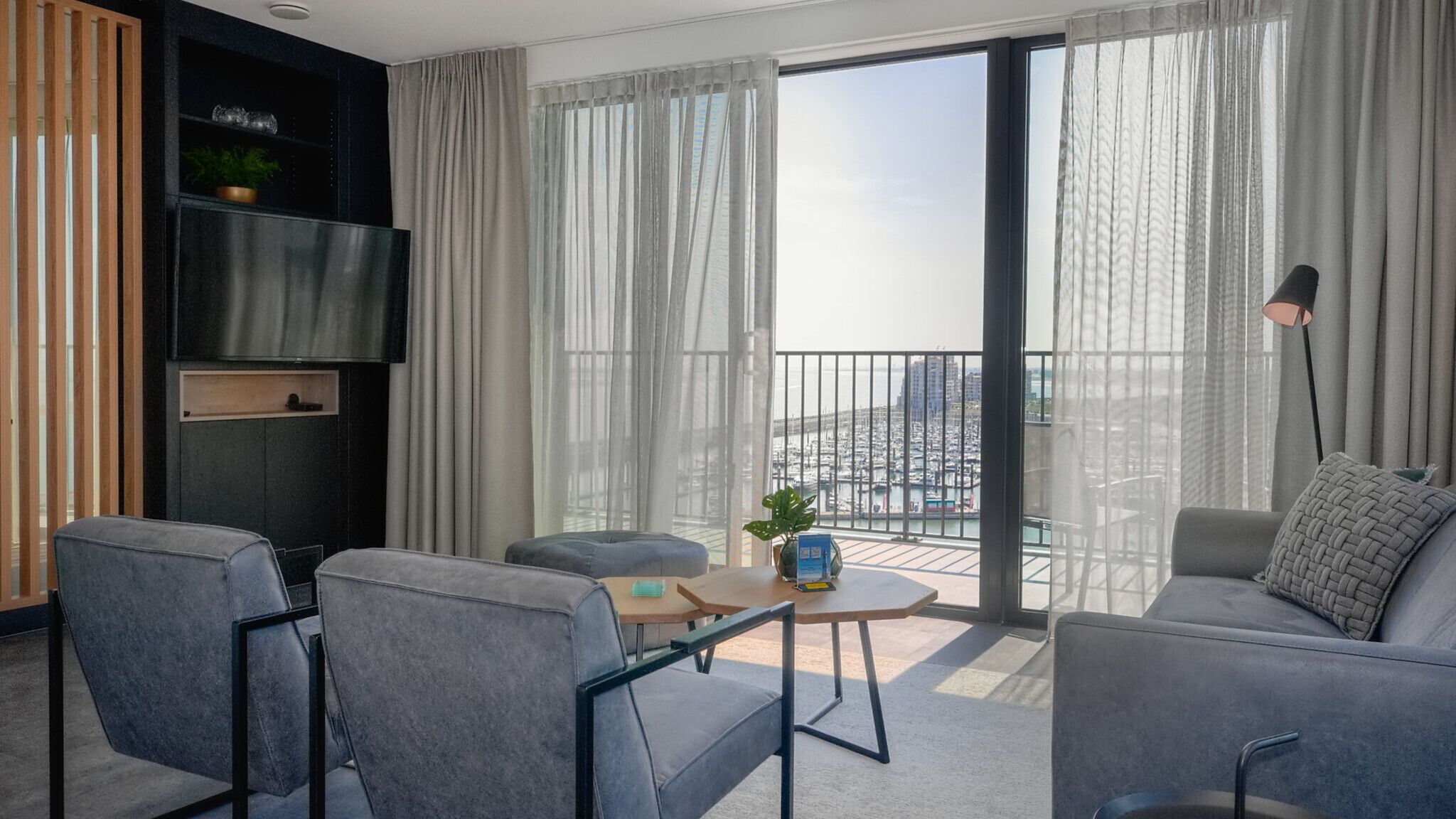 Una sala de estar moderna con un sofá, sillas, un televisor, una mesita y un balcón con vista a la ciudad.