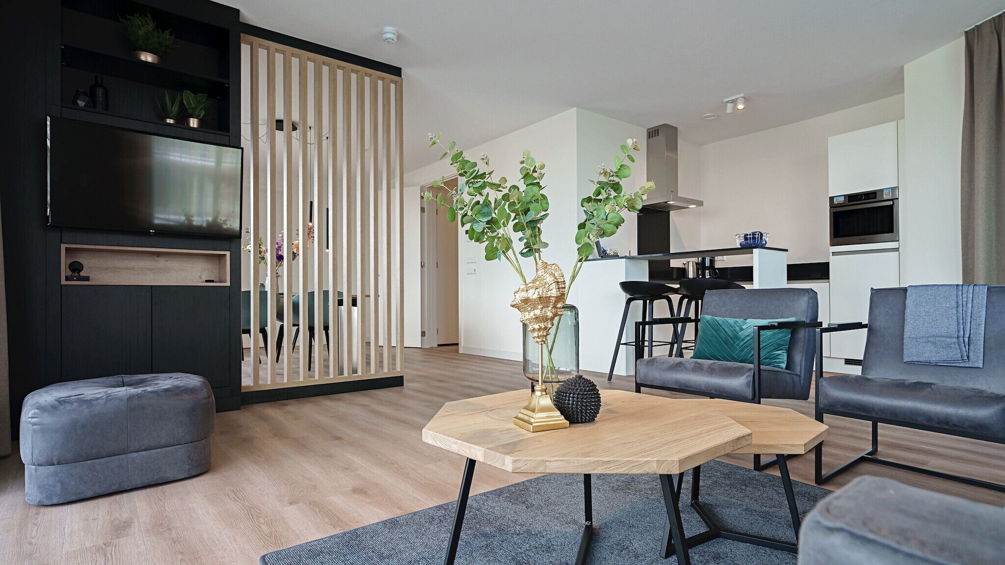 A modern living room with a sofa, two coffee tables, a decorative plant, and a kitchen area in the background.