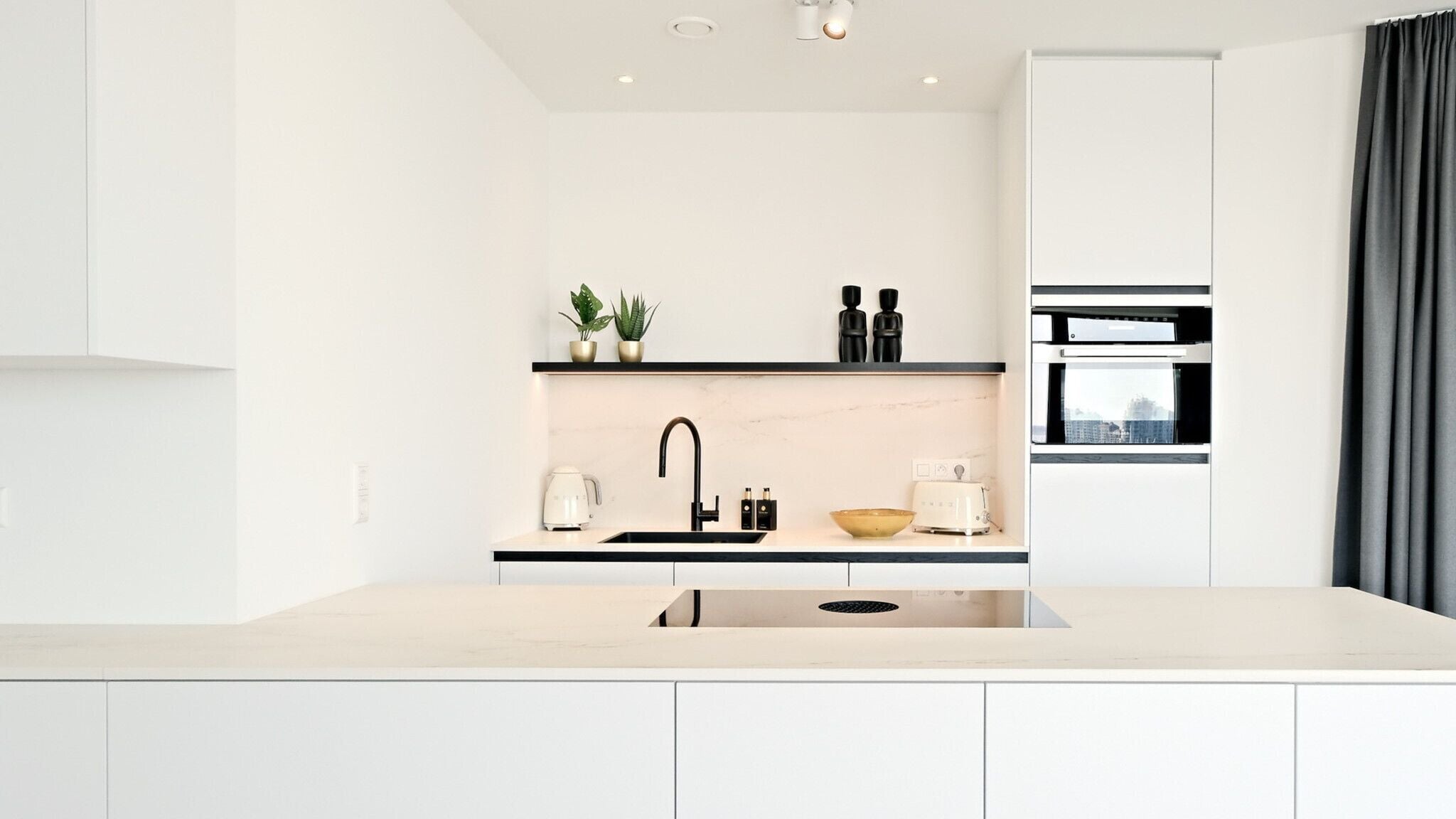 Een moderne keuken met een centraal eiland, een inbouwoven en een raam met uitzicht over de stad.