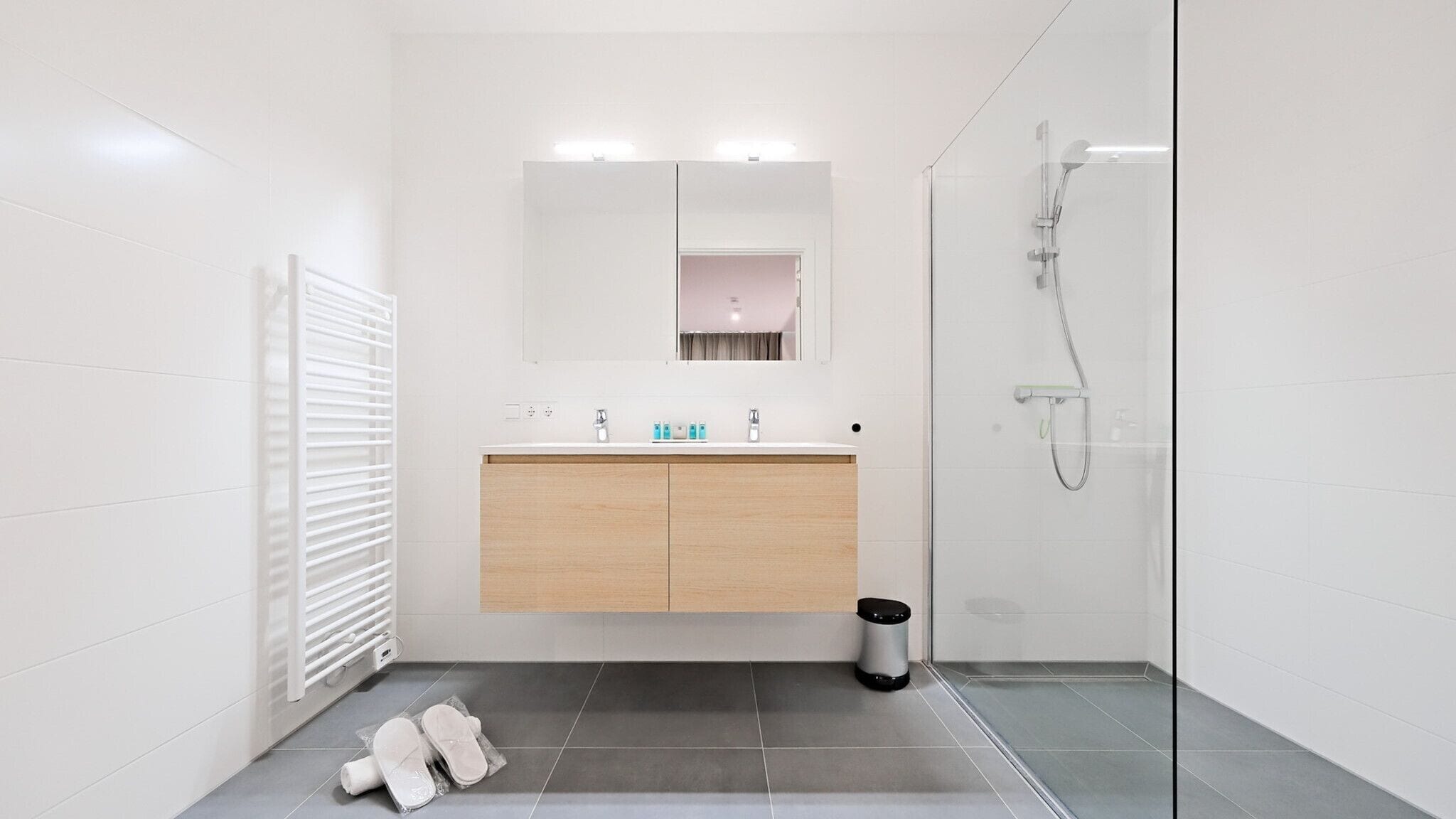 A modern bathroom with a glass shower enclosure, a wooden vanity, and a tiled floor.
