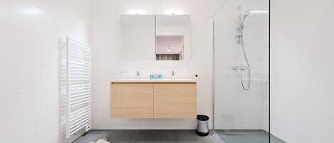A modern bathroom with a glass shower enclosure, a wooden vanity, and a tiled floor.