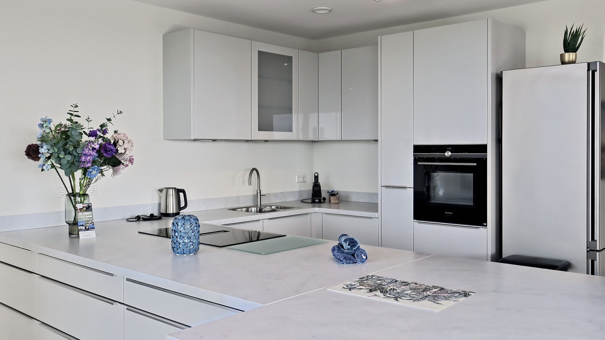 A modern kitchen with white cabinetry, a built-in oven, and a stainless steel refrigerator.