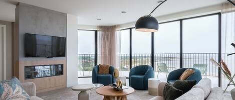 A modern living room with a large TV, comfortable seating, and a balcony with a view.