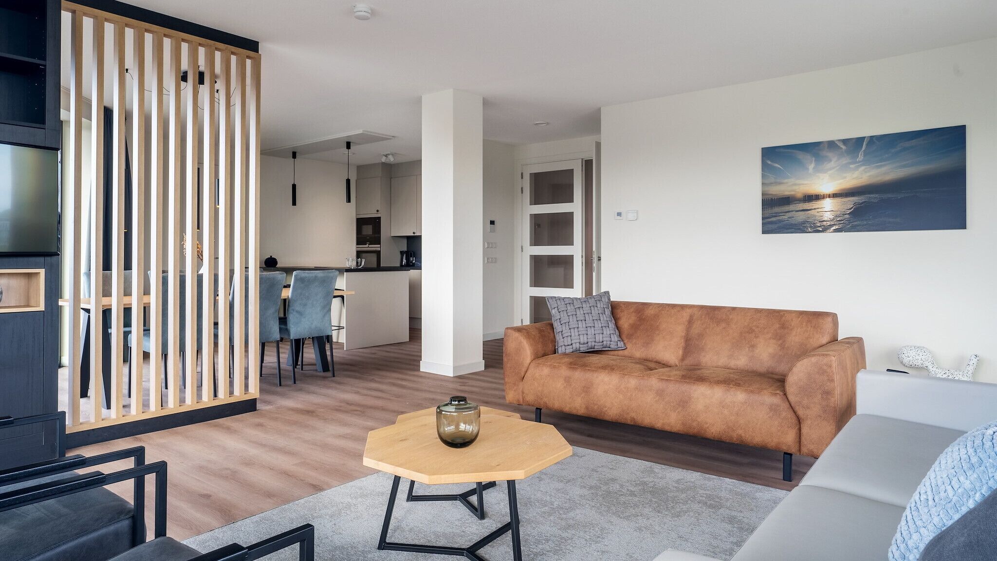 A modern living room with a brown sofa, a round coffee table, and a dining area with chairs.
