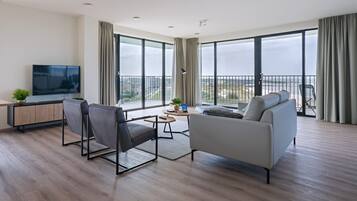 Un salon moderne avec un canapé, des fauteuils, un téléviseur et un balcon offrant une vue agréable.