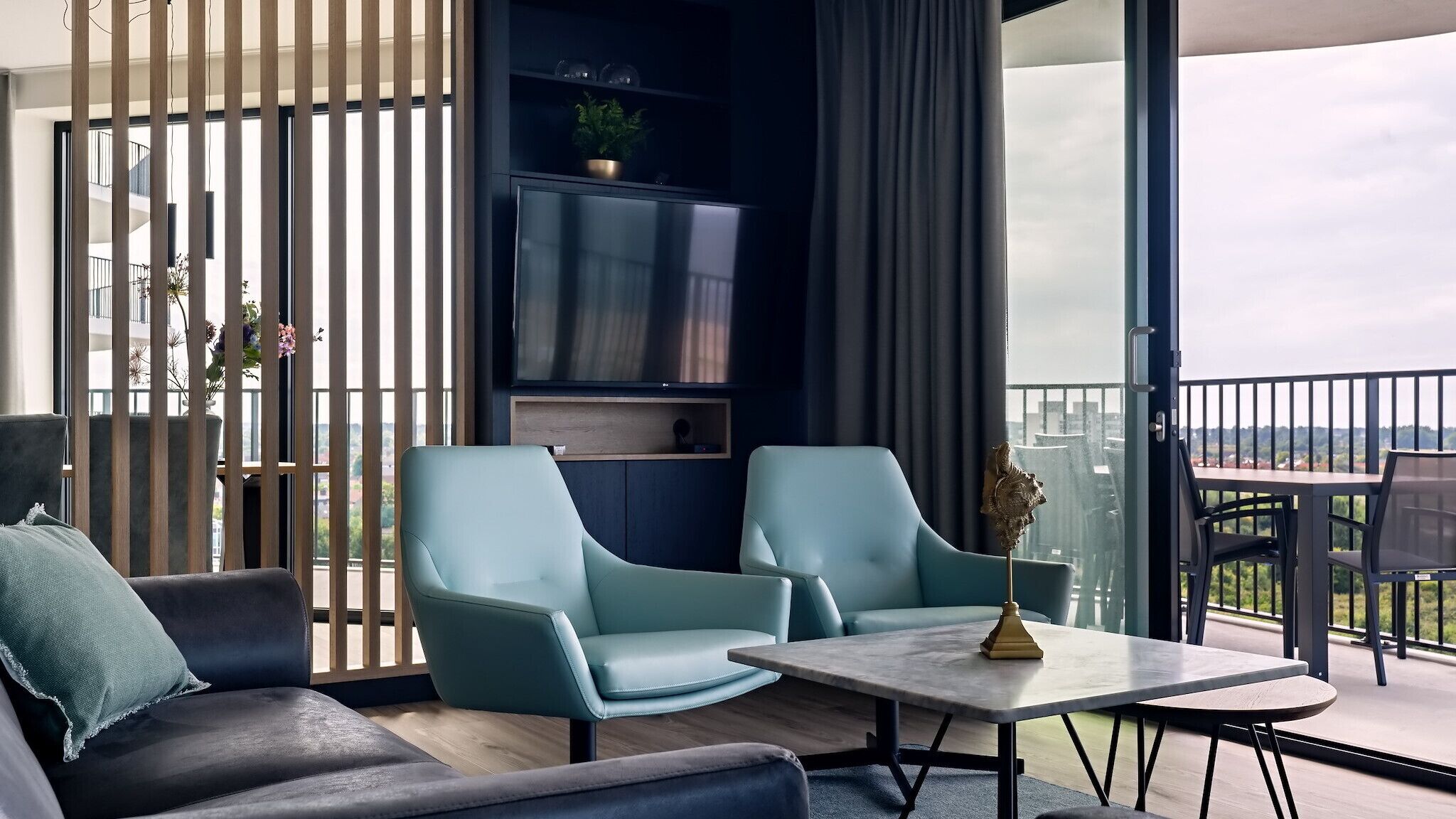Una sala moderna con un sofá, dos sillones, una mesita de centro y un televisor montado en la pared.