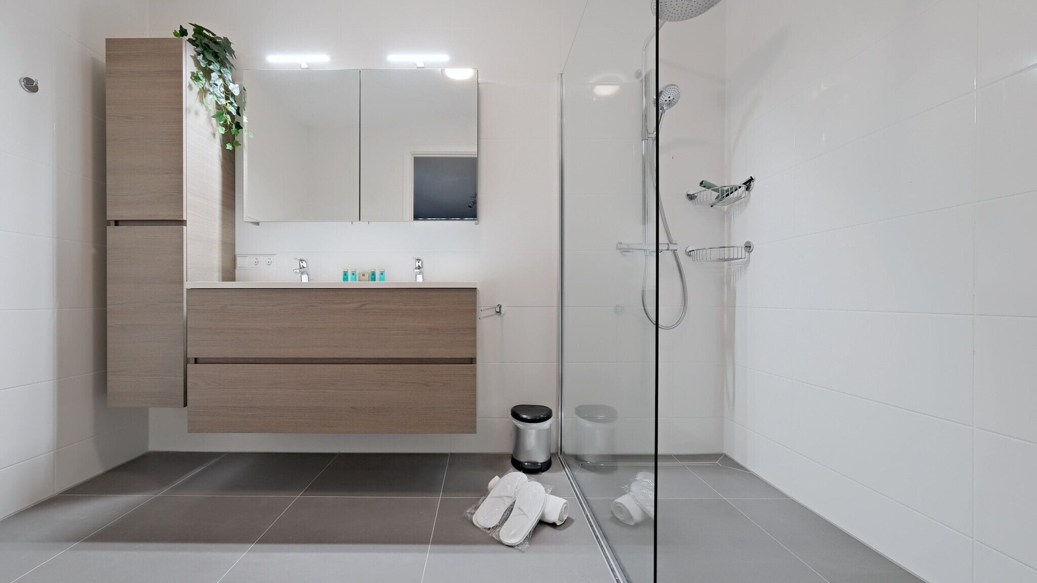 Un baño moderno con cabina de ducha de vidrio, tocador de madera y espejo sobre el lavabo.