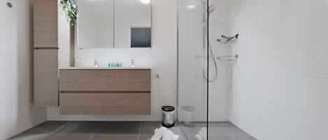Un baño moderno con cabina de ducha de vidrio, tocador de madera y espejo sobre el lavabo.
