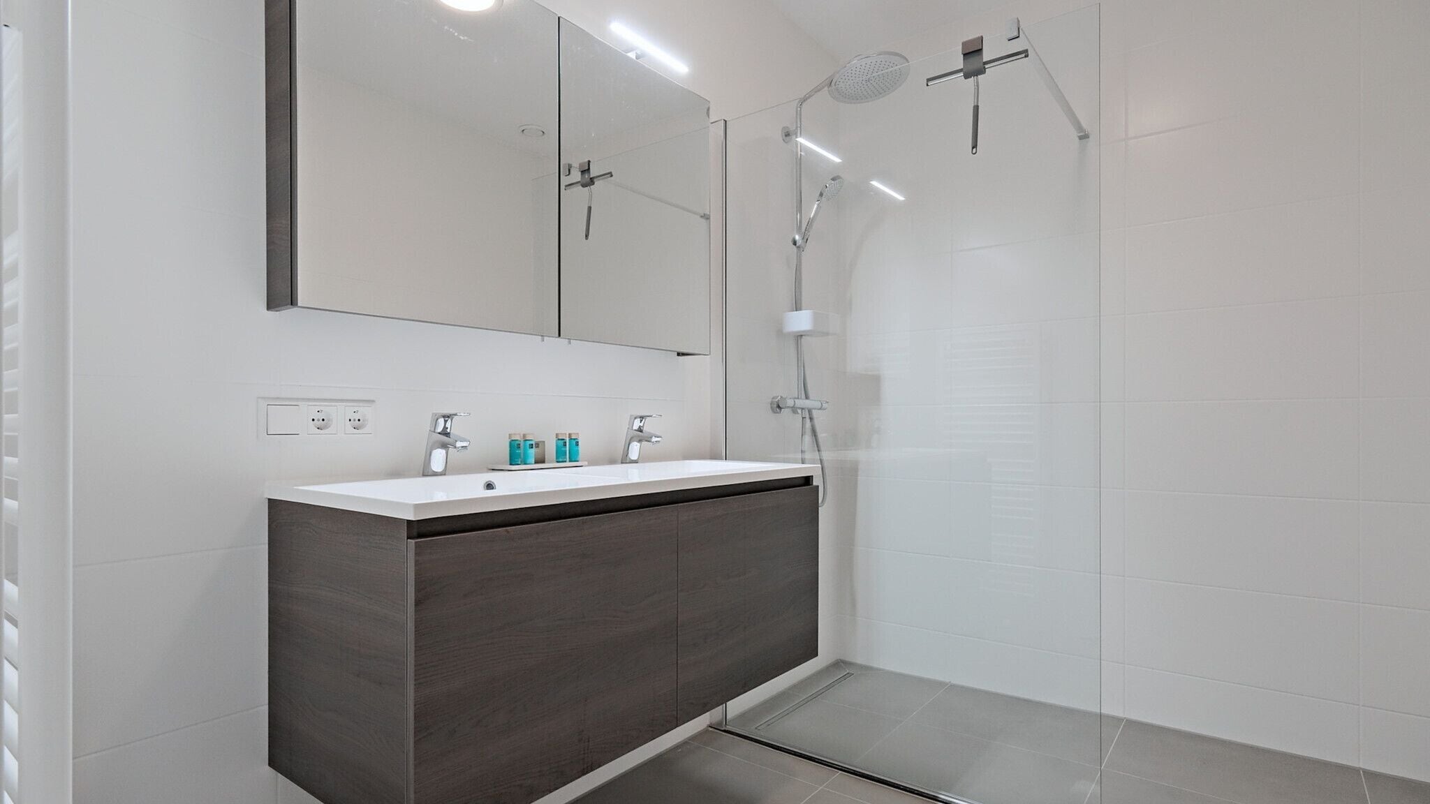 A modern bathroom with a large mirror, a vanity with a dark wood finish, a white sink, and a glass-enclosed shower area.