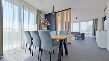 Un espace repas moderne avec une table en bois et des chaises grises, de grandes fenêtres et un vase décoratif rempli de fleurs.