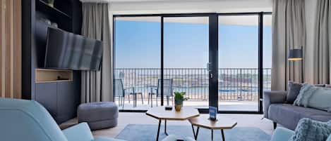 Un salon moderne doté d’un grand téléviseur, de sièges confortables, d’une petite table et d’un balcon offrant une vue sur la ville.
