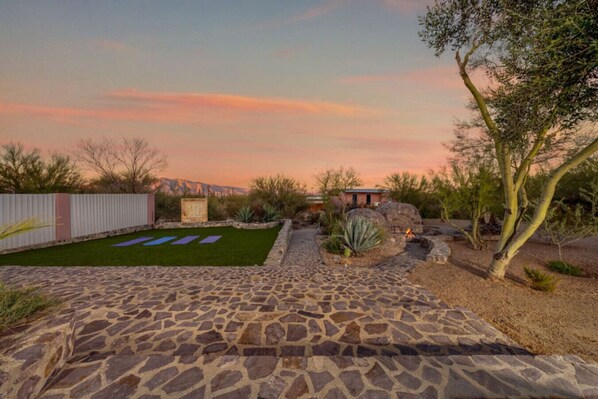 A backyard with a stone patio, a grassy lawn, and a small fire pit area.
