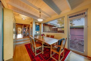 A dining area with a wooden table and chairs, a red patterned rug, and a large window with a view of the outside.