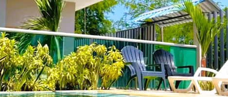 A pool area with clear blue water, surrounded by greenery and modern outdoor furniture.