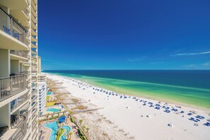 Un hôtel de grande hauteur offrant une vue sur la plage, avec un espace piscine et une plage de sable dotée de parasols.