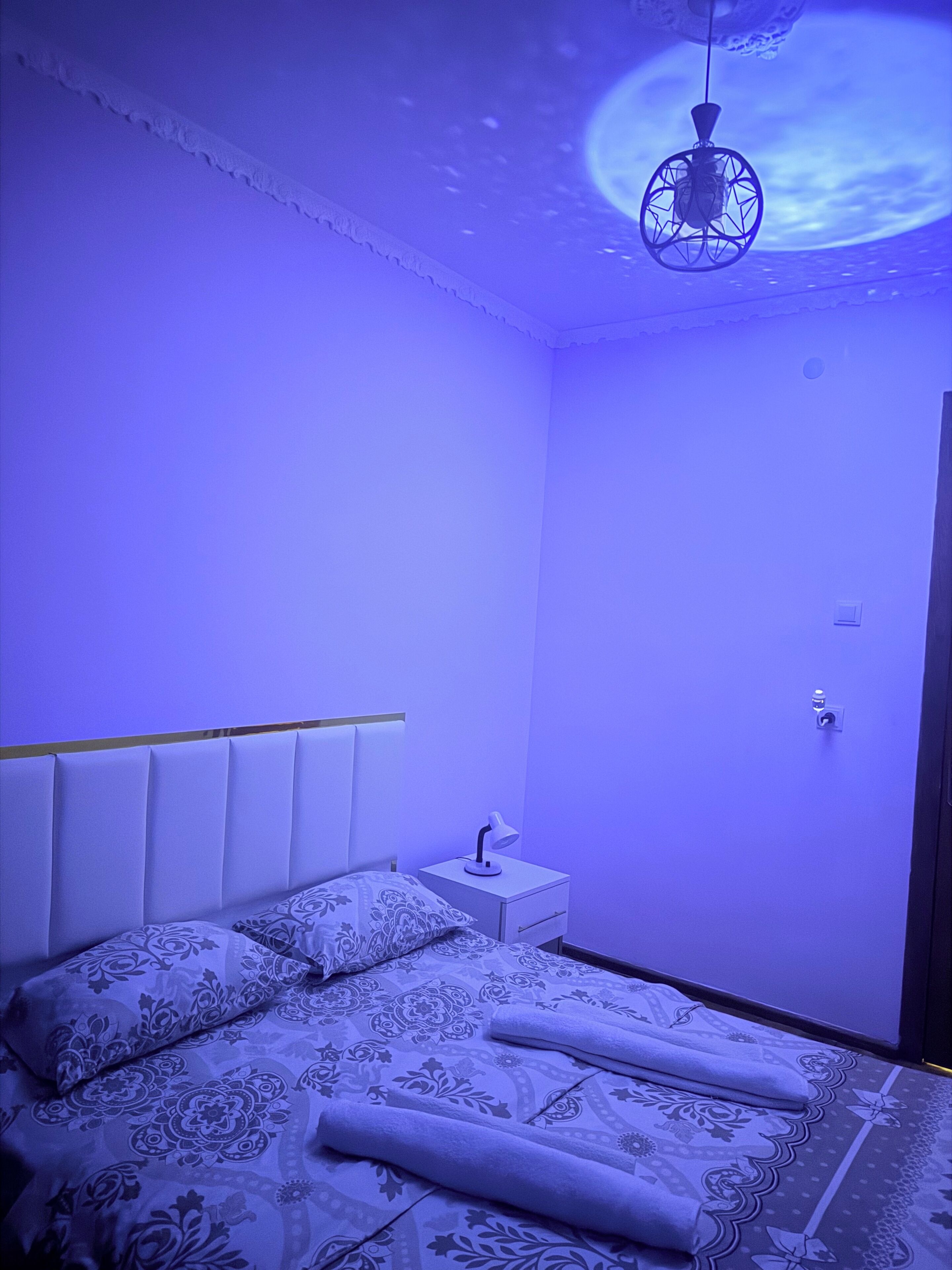 Un dormitorio con cama, mesita de noche y lámpara colgante.