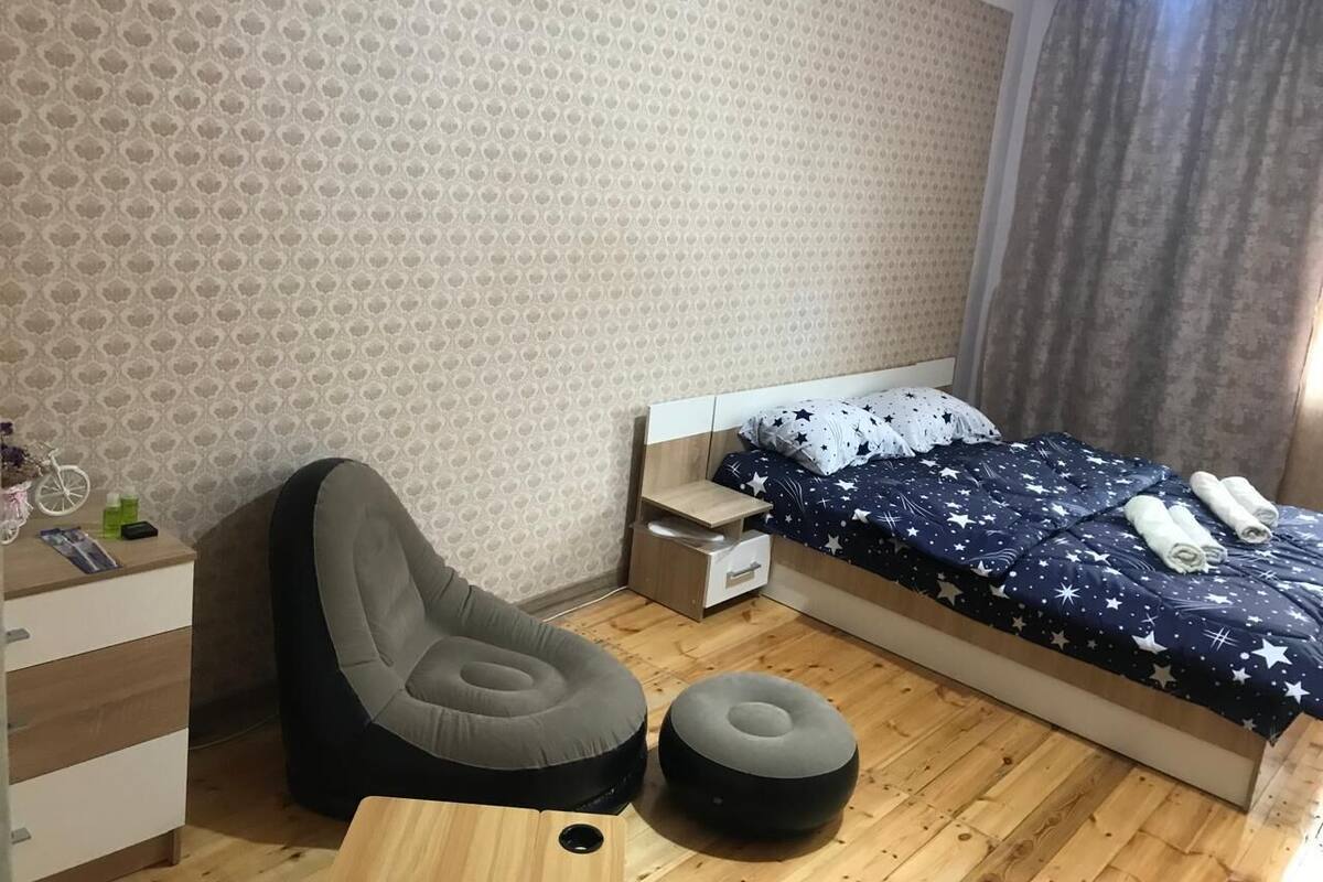 A bedroom with a bed, a chair, a nightstand, and a dresser.