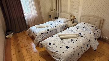 A room with two beds, wooden flooring, a mirror, and a hanging light fixture.