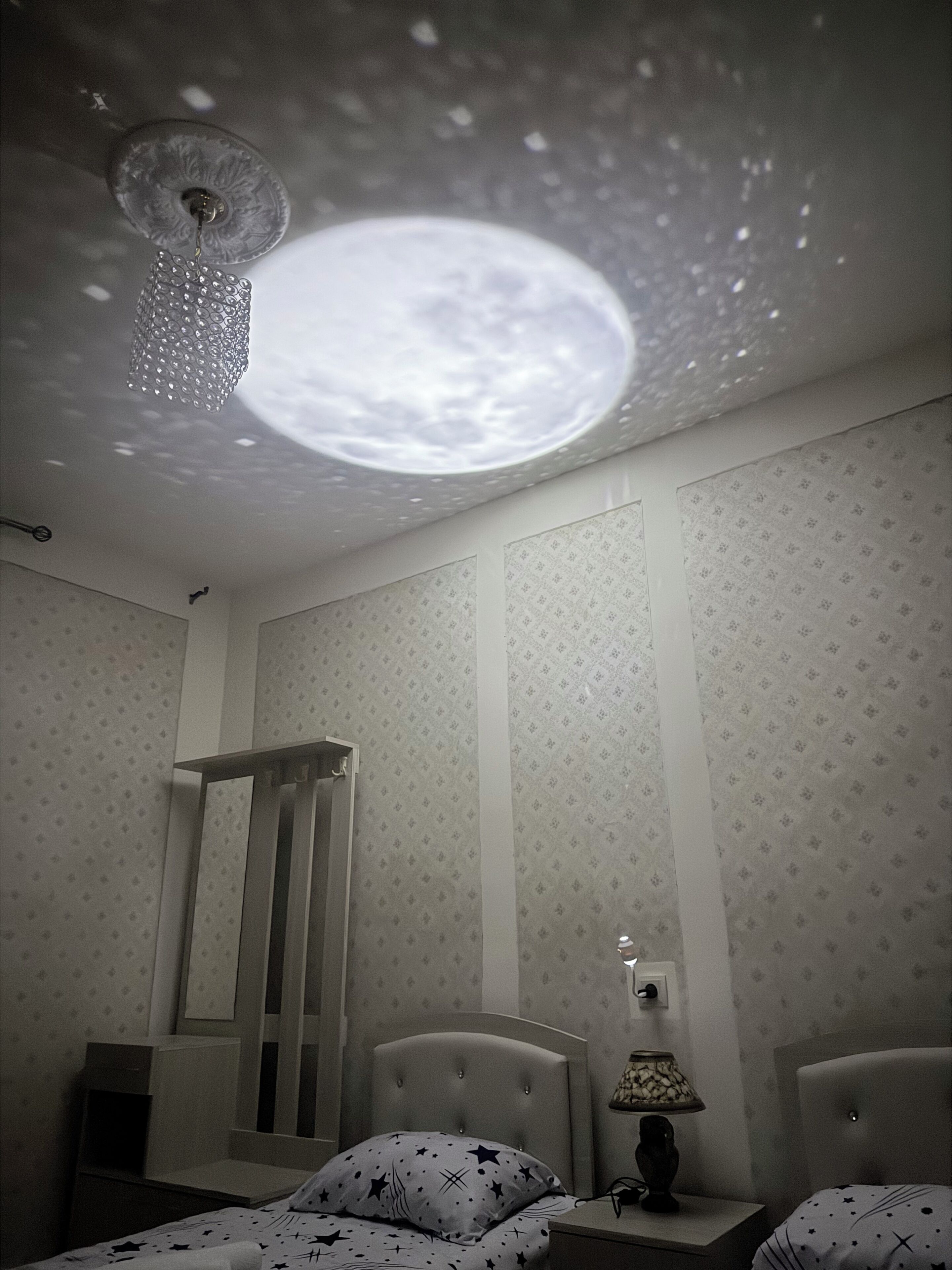 Een slaapkamer met een bed, nachtkastje, lamp en een plafondlamp.