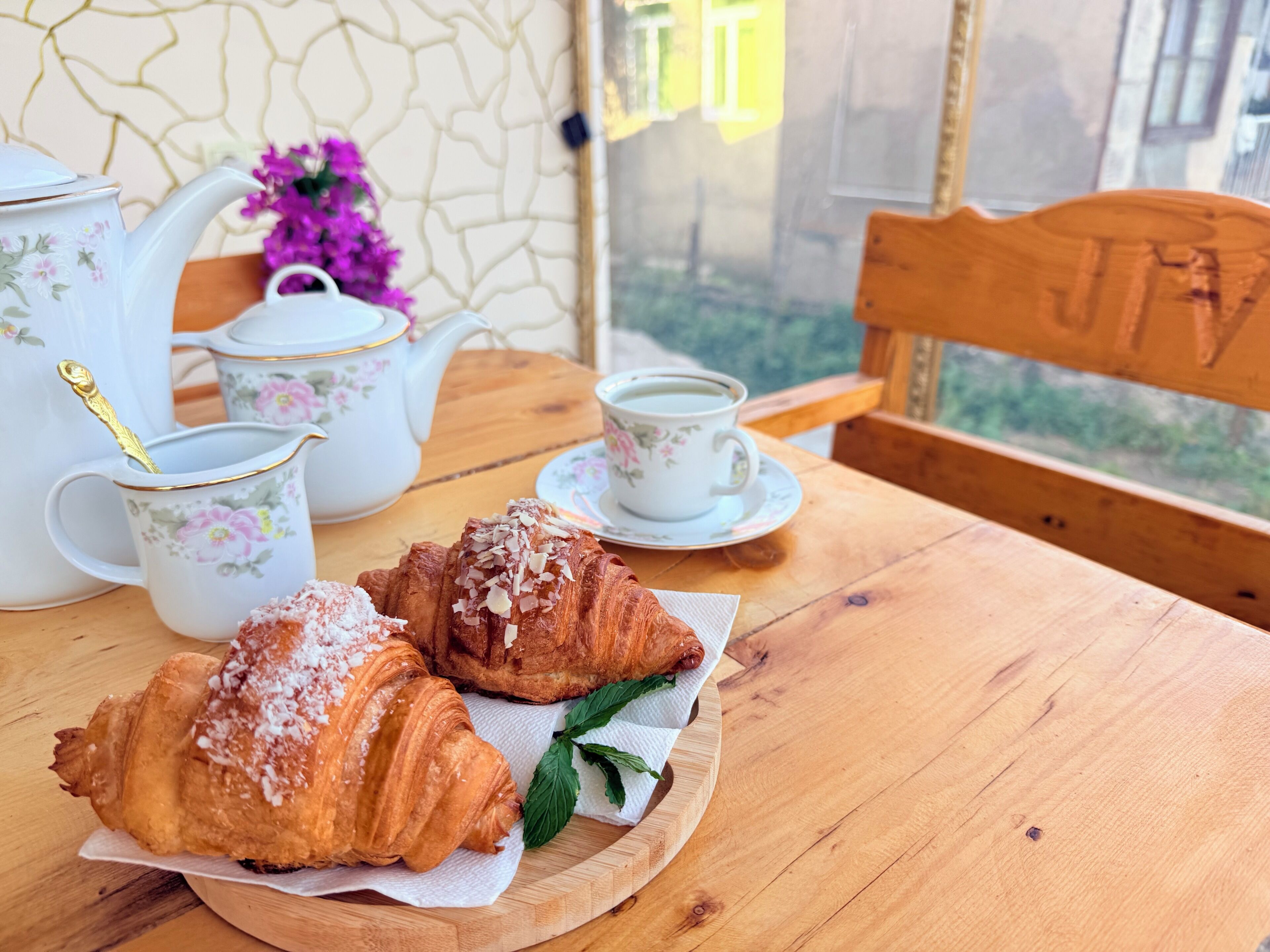 A wooden table with a tea set, two pastries, and a vase of flowers.