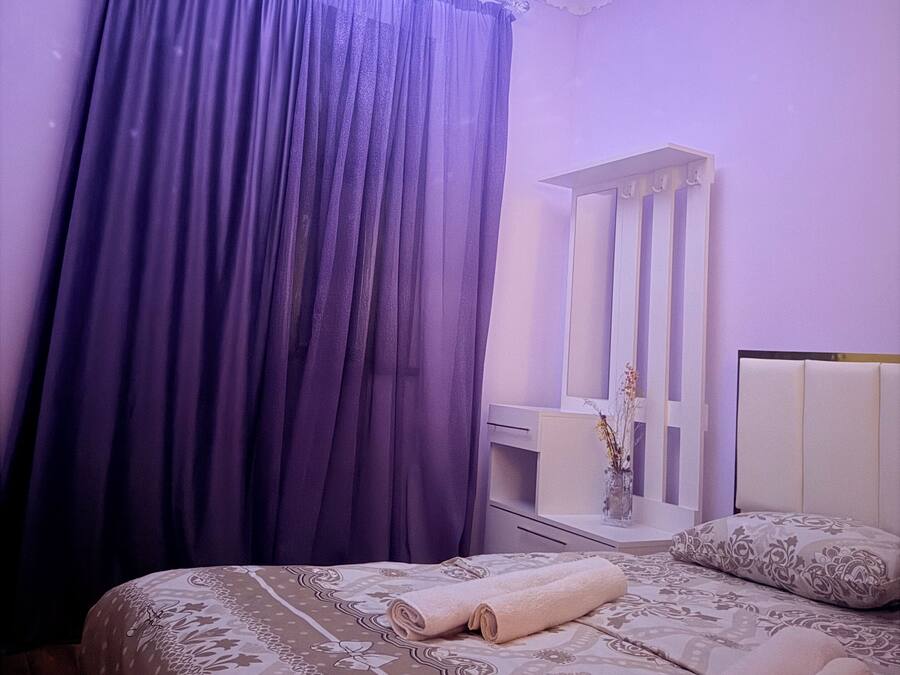 A bedroom with a bed, a mirror, and a window with purple curtains.